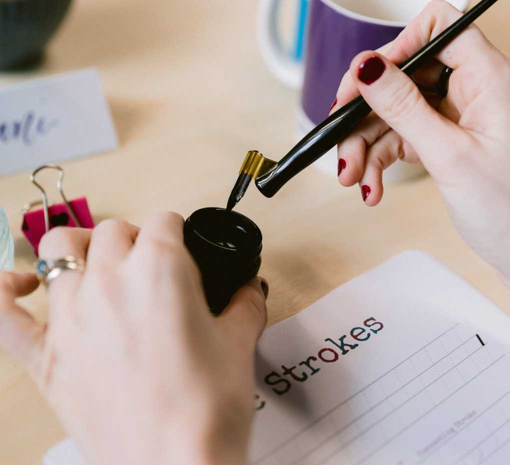dani Brushfield-Smith dipping a calligraphy pen into black ink